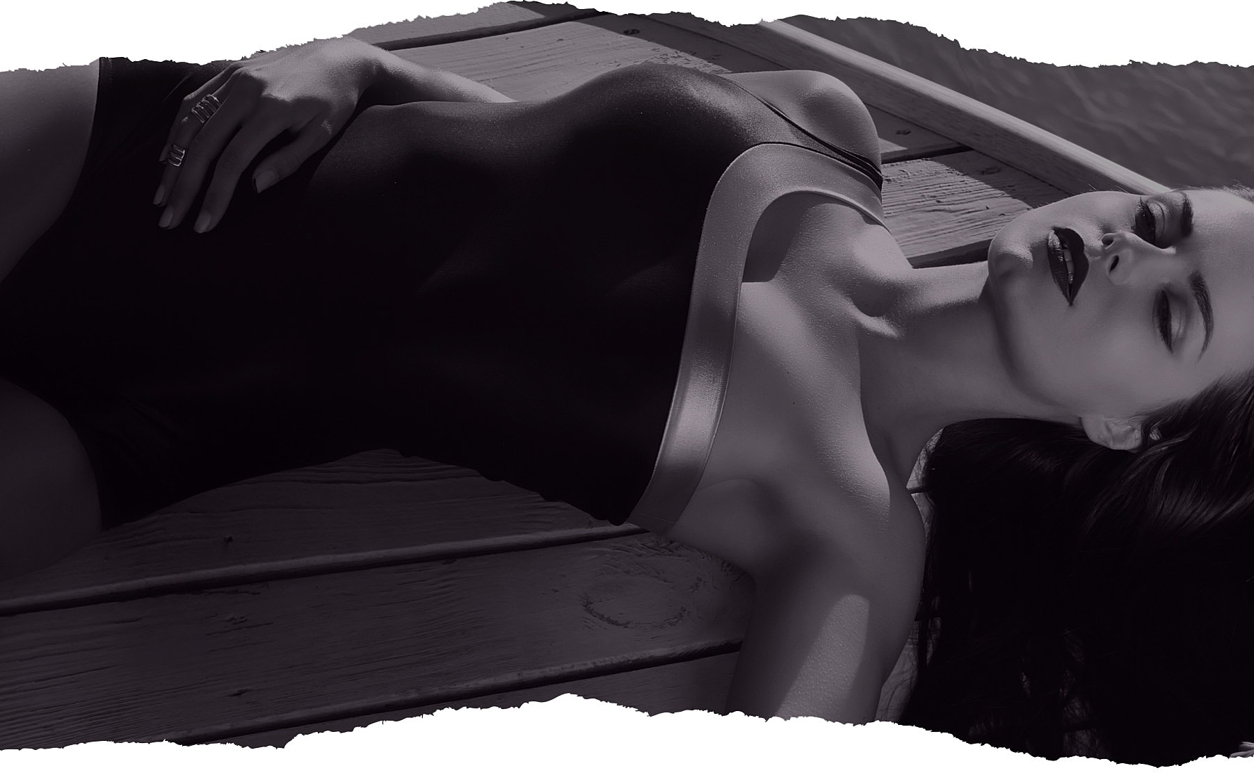 Model in black swimsuit lounging on dock.