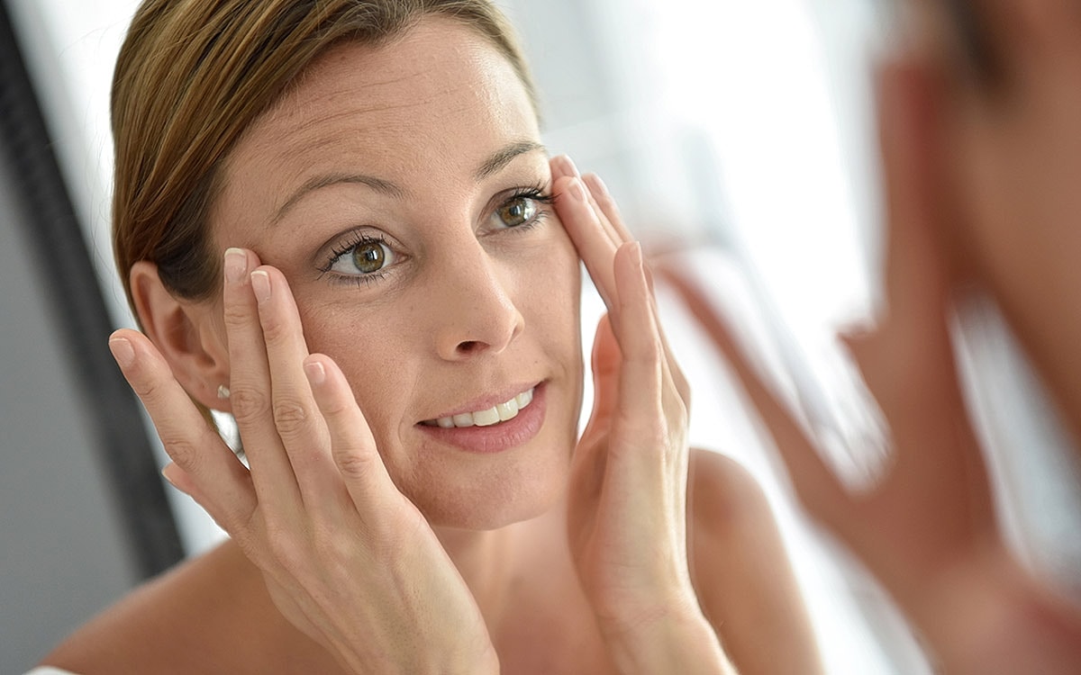 Woman applying skincare in mirror reflection.