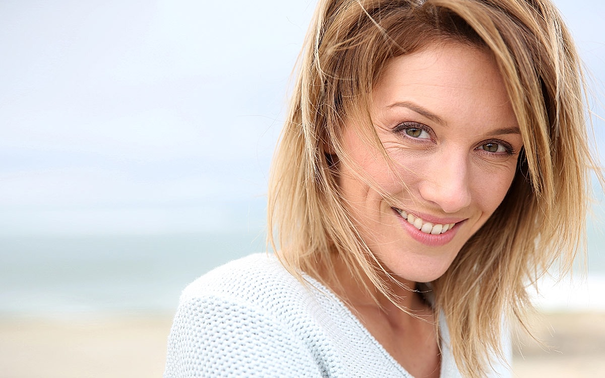 Smiling woman with long hair at the beach.