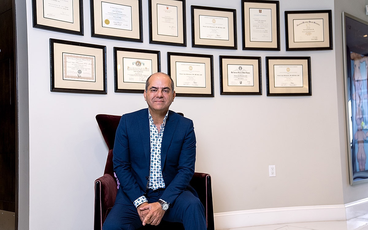 Dr. Siamak Agha seated with framed certificates behind.