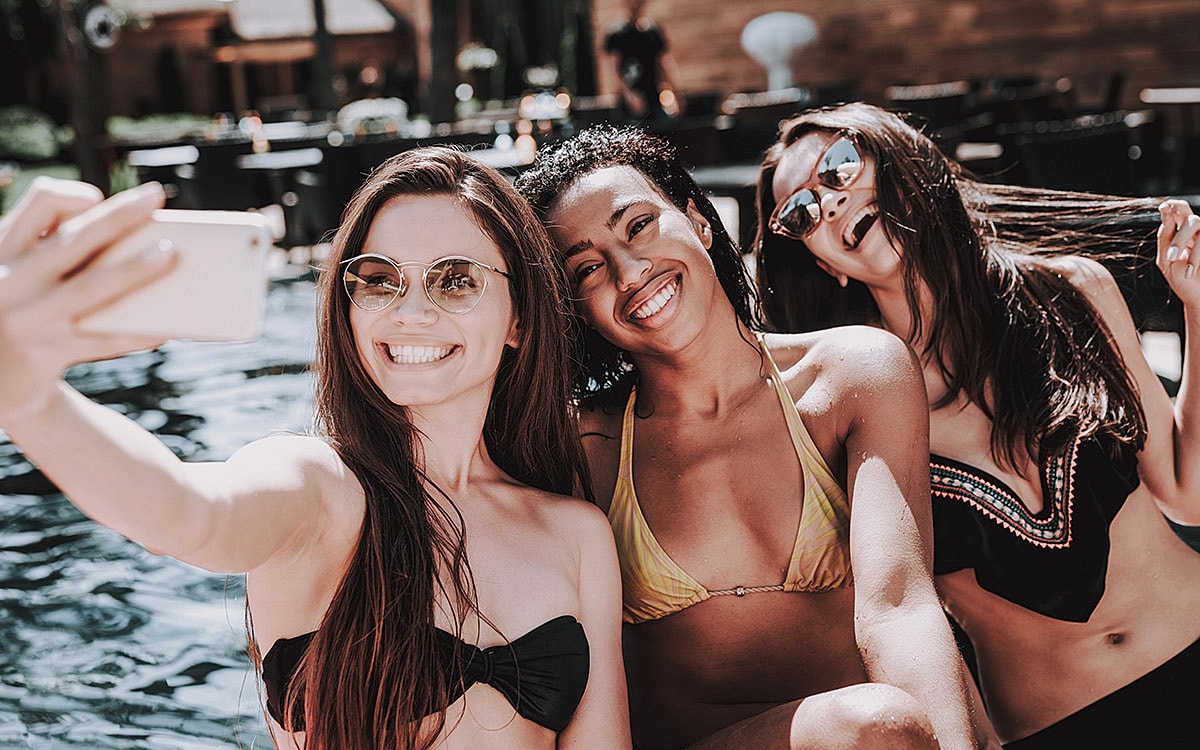 Friends taking selfies by the pool.