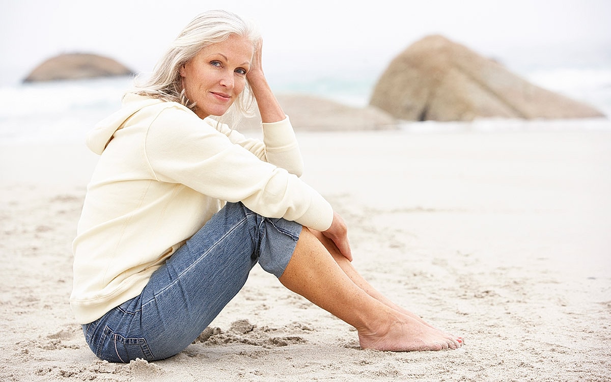 Woman sitting on beach, looking thoughtful.
