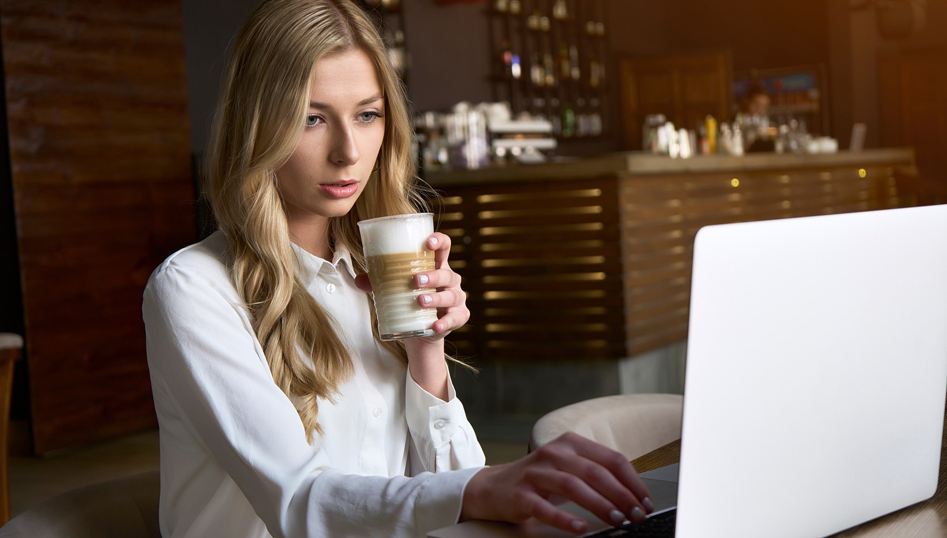 Woman with coffee working on laptop in cafe.