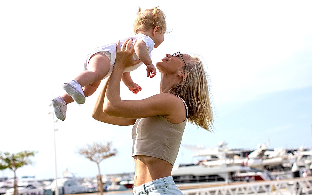 Mother playfully lifting her baby outdoors.