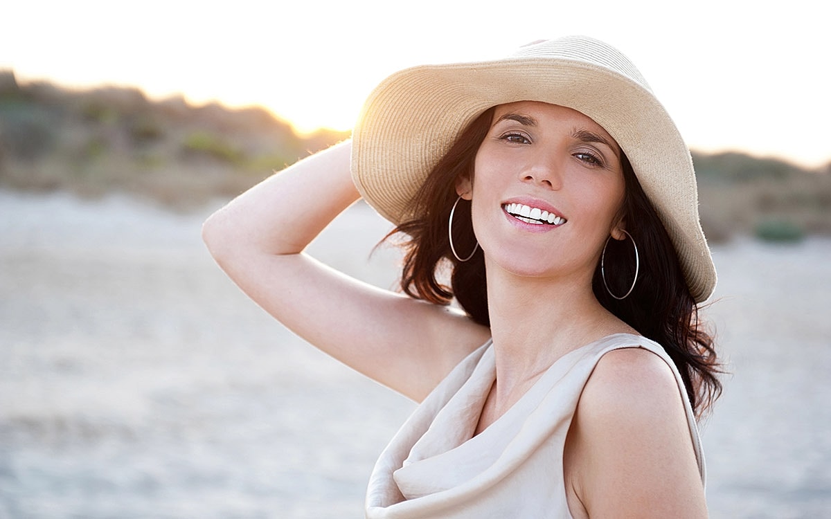 Smiling woman wearing hat by the beach.
