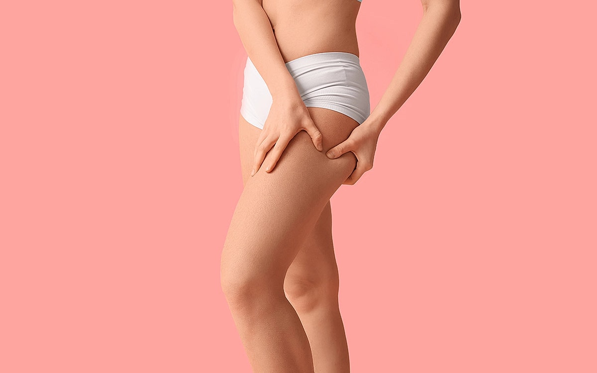Woman holding thigh against a pink background.