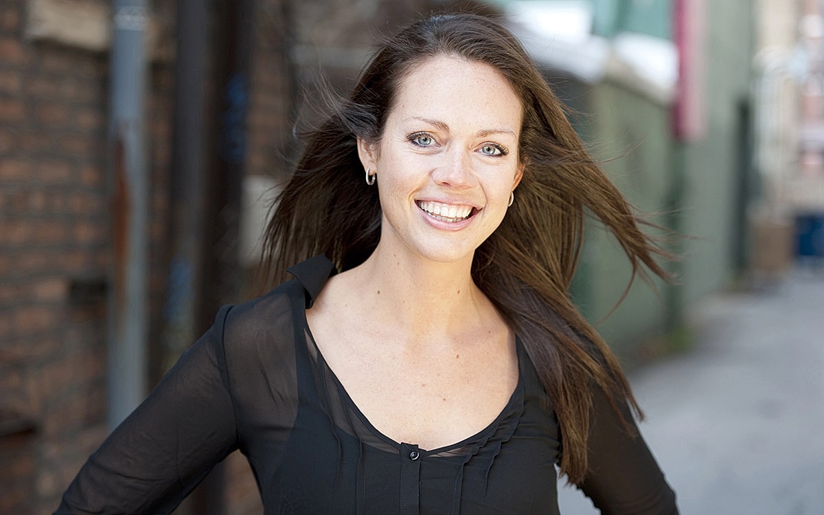 Smiling woman with flowing hair in urban setting.