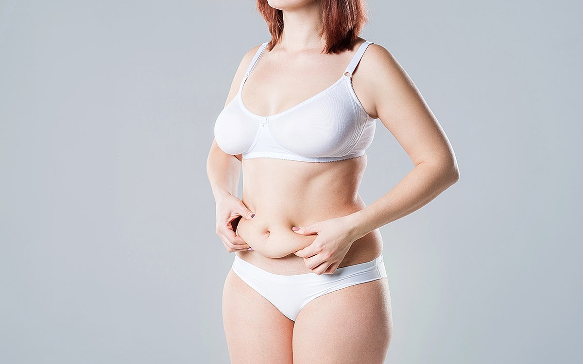 Woman in underwear examining her stomach.
