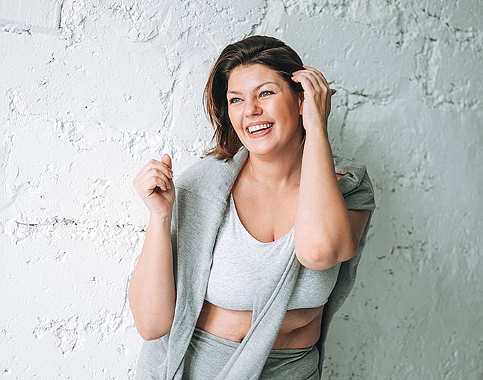 Smiling woman in gray outfit against white wall.